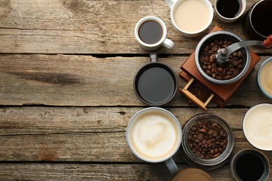 Different coffee drinks in cups, beans and manual grinder on wooden table, flat lay. Space for text