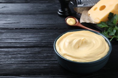 Photo of Tasty cheese sauce in bowl on black wooden table, space for text