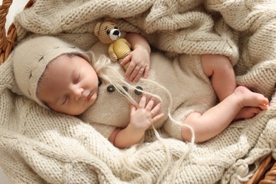 Photo of Adorable newborn baby with toy bear sleeping in wicker basket, top view