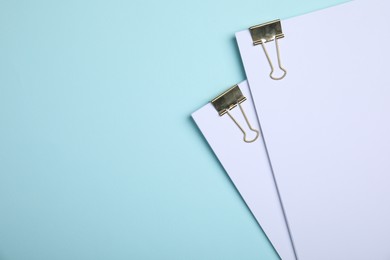 Sheets of paper with clips on light blue background, top view