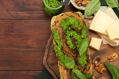 Photo of Freshly baked pesto bread with basil and cheese on wooden table, flat lay. Space for text