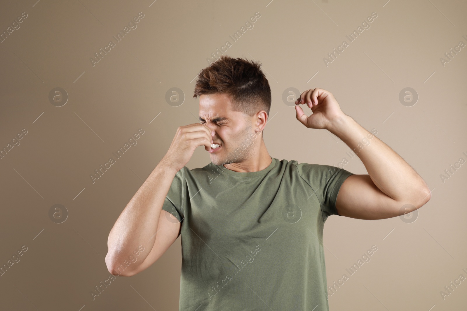 Photo of Young man with sweat stain on his clothes against beige background. Using deodorant