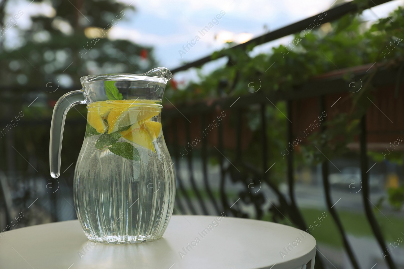 Photo of Jug with refreshing lemon water on light table outdoors. Space for text