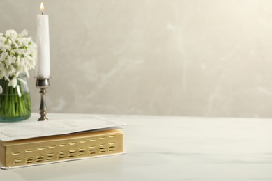 Burning church candle, Bible and flowers on white marble table. Space for text