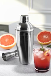 Metal shaker, delicious cocktail, jigger and grapefruit on light grey table