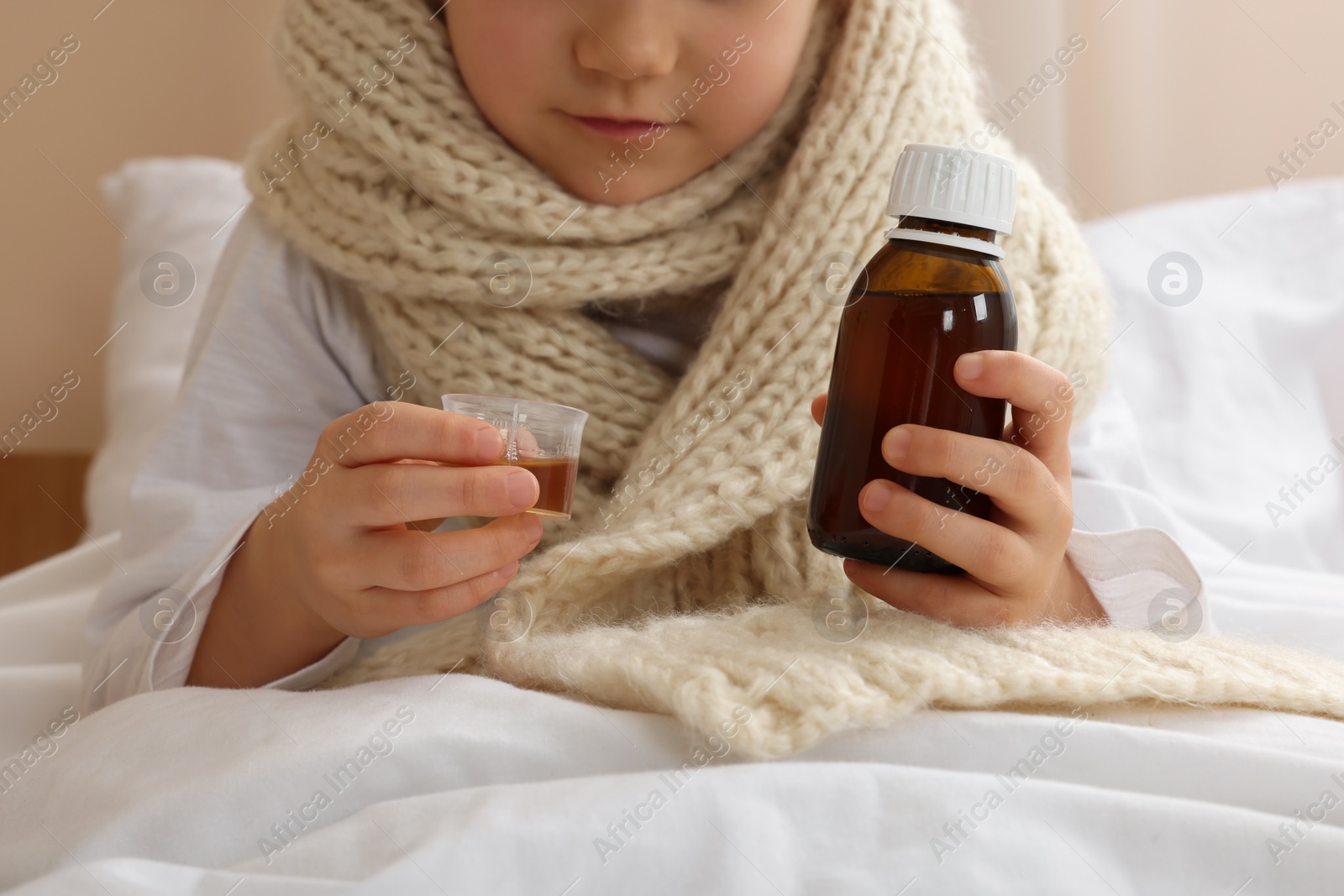 Photo of Sick girl taking cough syrup on bed at home, closeup. Cold medicine