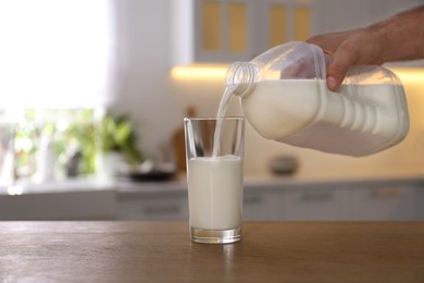 Man pouring milk from gallon bottle into glass at wooden table in kitchen, closeup