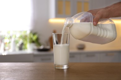 Photo of Man pouring milk from gallon bottle into glass at wooden table in kitchen, closeup