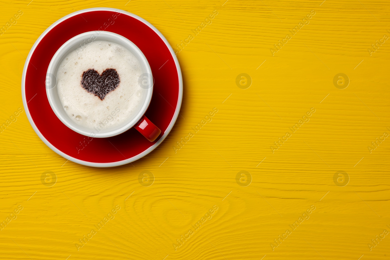 Photo of Cup of aromatic coffee with heart shaped decoration on yellow wooden table, top view. Space for text