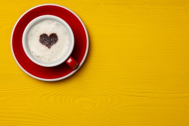 Cup of aromatic coffee with heart shaped decoration on yellow wooden table, top view. Space for text