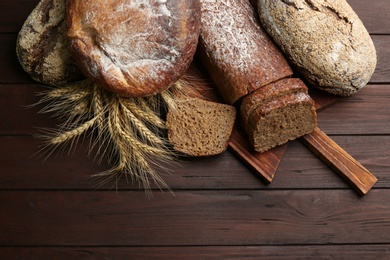 Photo of Different kinds of fresh bread on wooden table, flat lay
