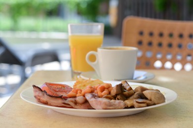 Photo of Delicious breakfast with fried meat and vegetables served on beige table in cafe, closeup