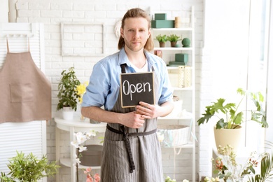 Photo of Male florist holding OPEN sign at workplace