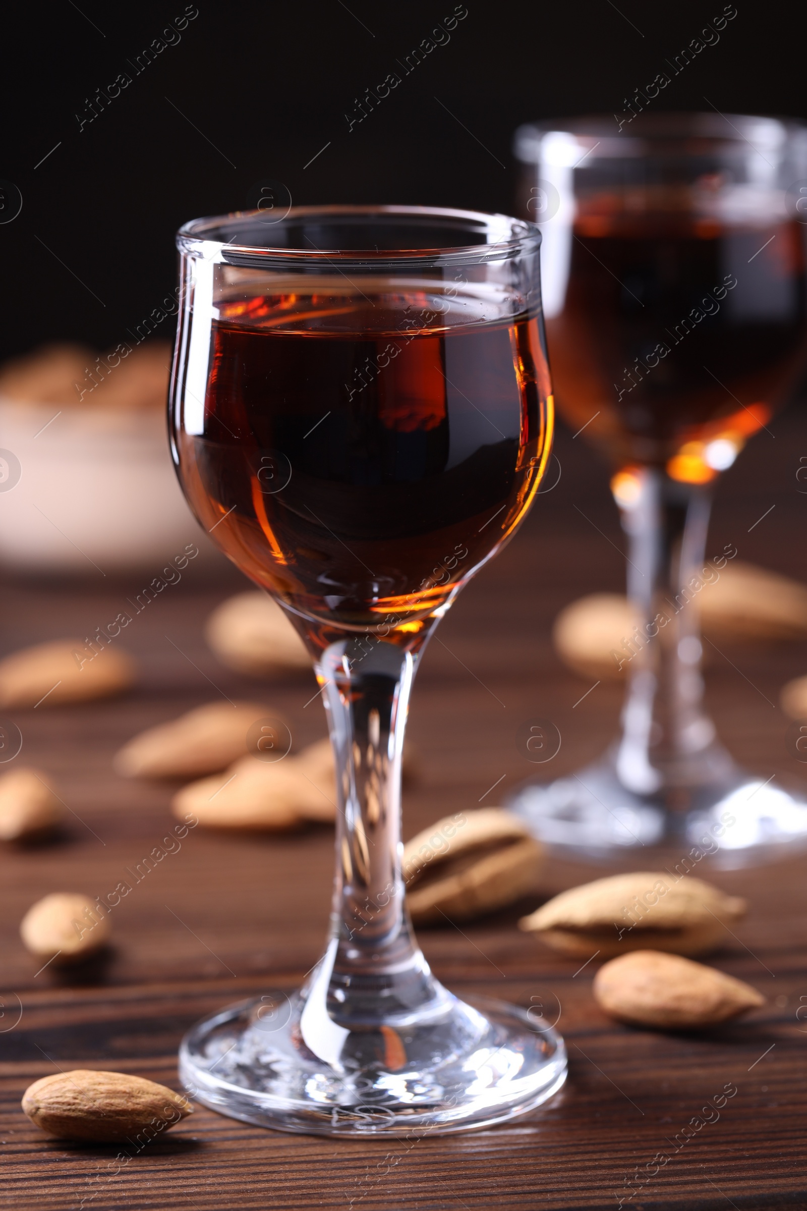 Photo of Liqueur glass with tasty amaretto and almonds on wooden table, closeup