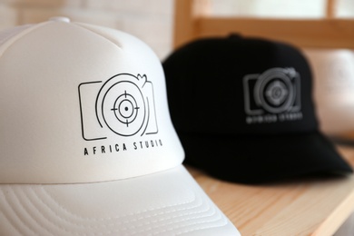 Photo of Caps with logo on wooden shelf in shop, closeup