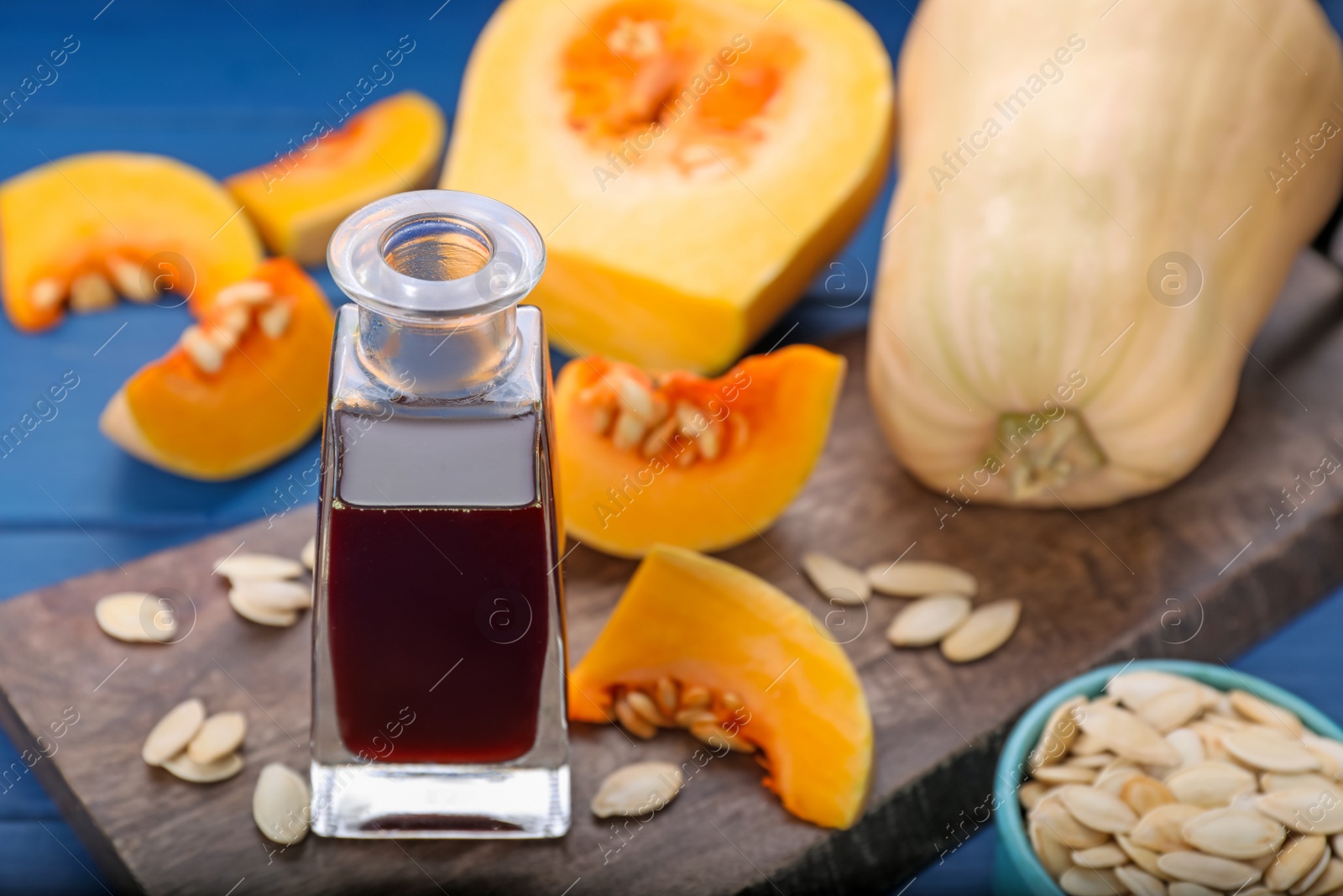 Photo of Fresh pumpkin seed oil in glass bottle on blue wooden table