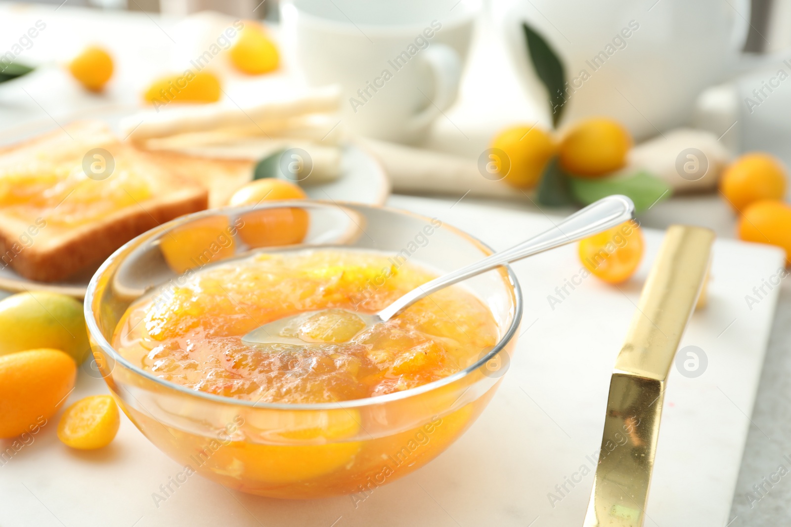 Photo of Delicious kumquat jam in glass bowl on white tray, closeup