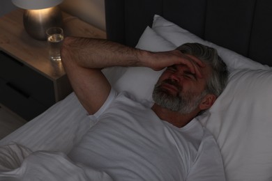 Mature man suffering from headache in bed at night