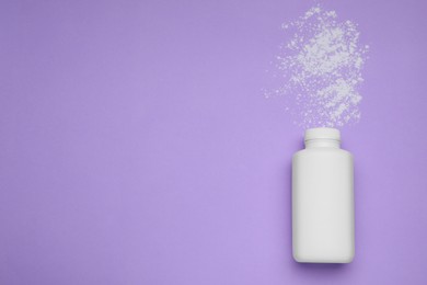 Bottle and scattered dusting powder on violet background, top view with space for text. Baby cosmetic product