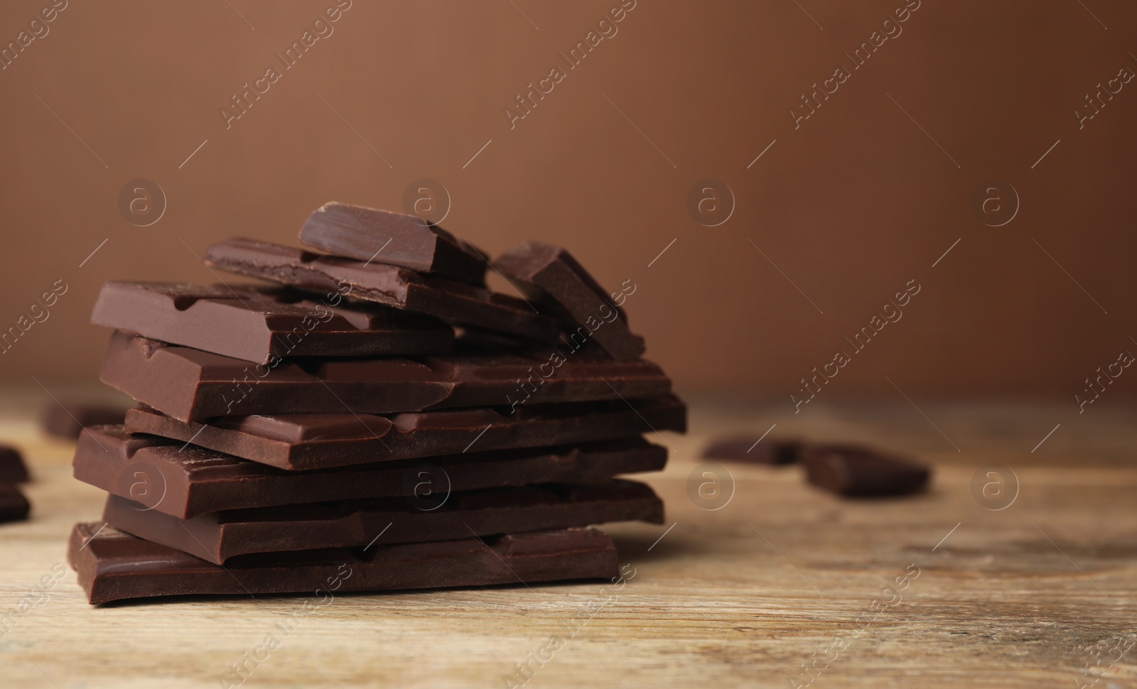 Photo of Pieces of tasty chocolate on wooden table, closeup. Space for text