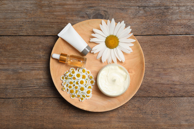 Photo of Composition with chamomile flowers and cosmetic products on wooden table, top view