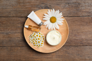 Composition with chamomile flowers and cosmetic products on wooden table, top view