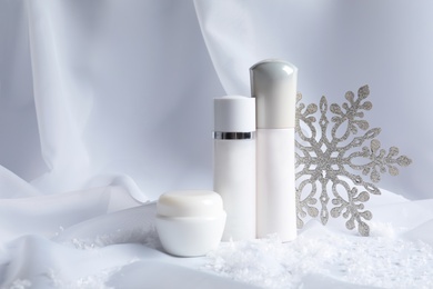 Photo of Set of cosmetic products and decorative snow on white fabric, space for text. Winter care