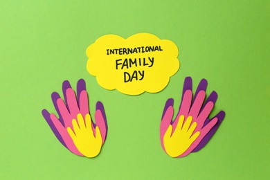 Photo of Paper palms and card with text International Family Day on light green background, flat lay