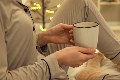 Woman in grey pajama holding cup of coffee indoors, closeup