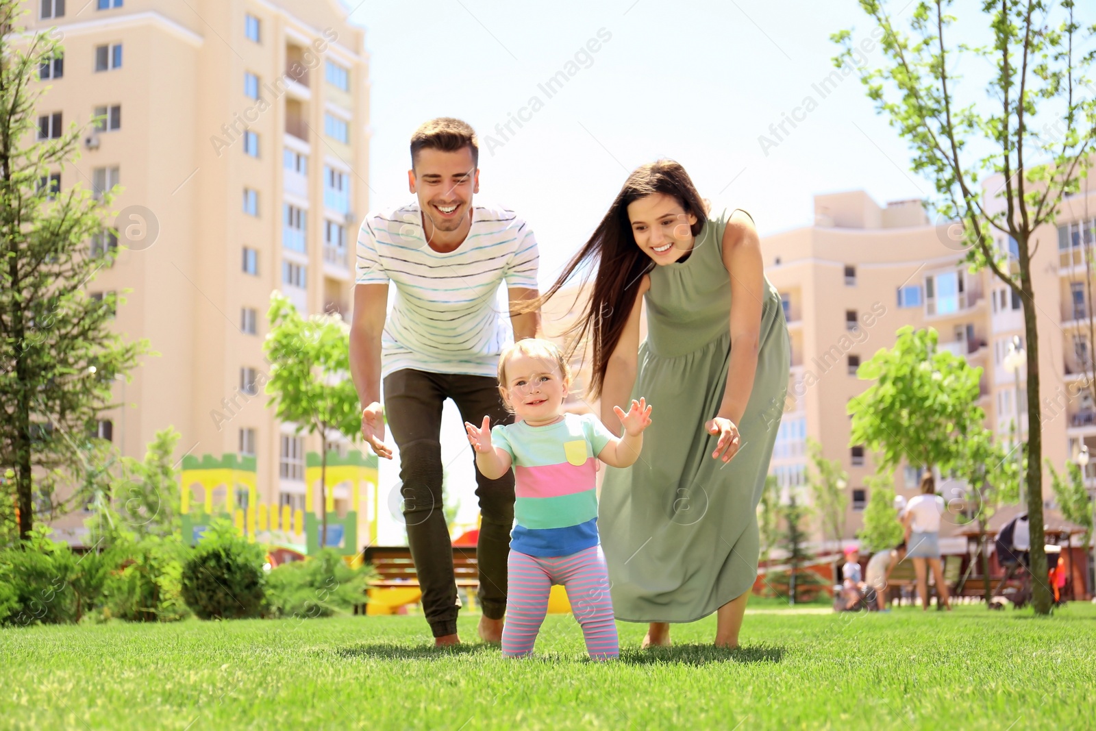Photo of Parents supporting their baby daughter while she learning to walk outdoors