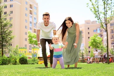 Photo of Parents supporting their baby daughter while she learning to walk outdoors