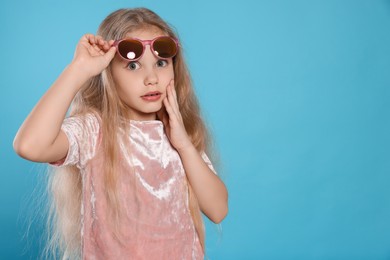 Excited girl wearing stylish sunglasses on light blue background, space for text