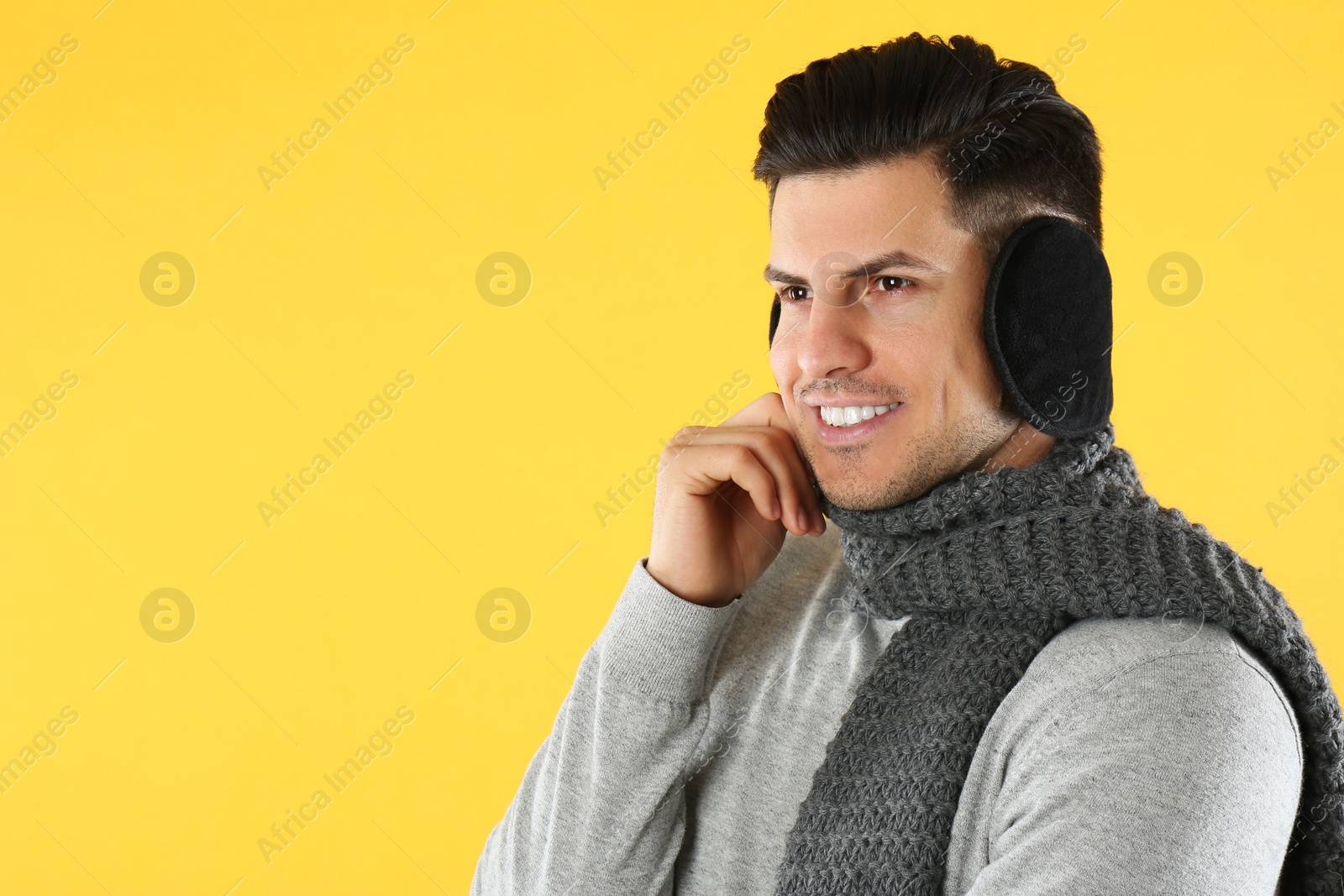 Photo of Man wearing stylish earmuffs and scarf on yellow background. Space for text