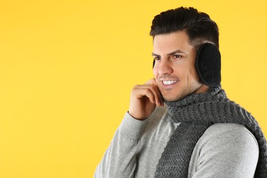 Photo of Man wearing stylish earmuffs and scarf on yellow background. Space for text