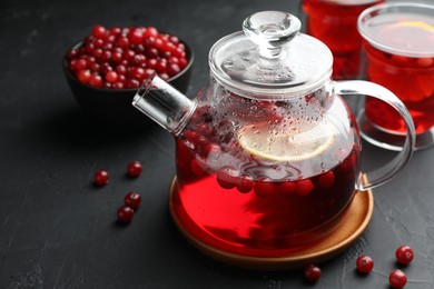 Tasty hot cranberry tea with lemon in teapot and fresh berries on black textured table