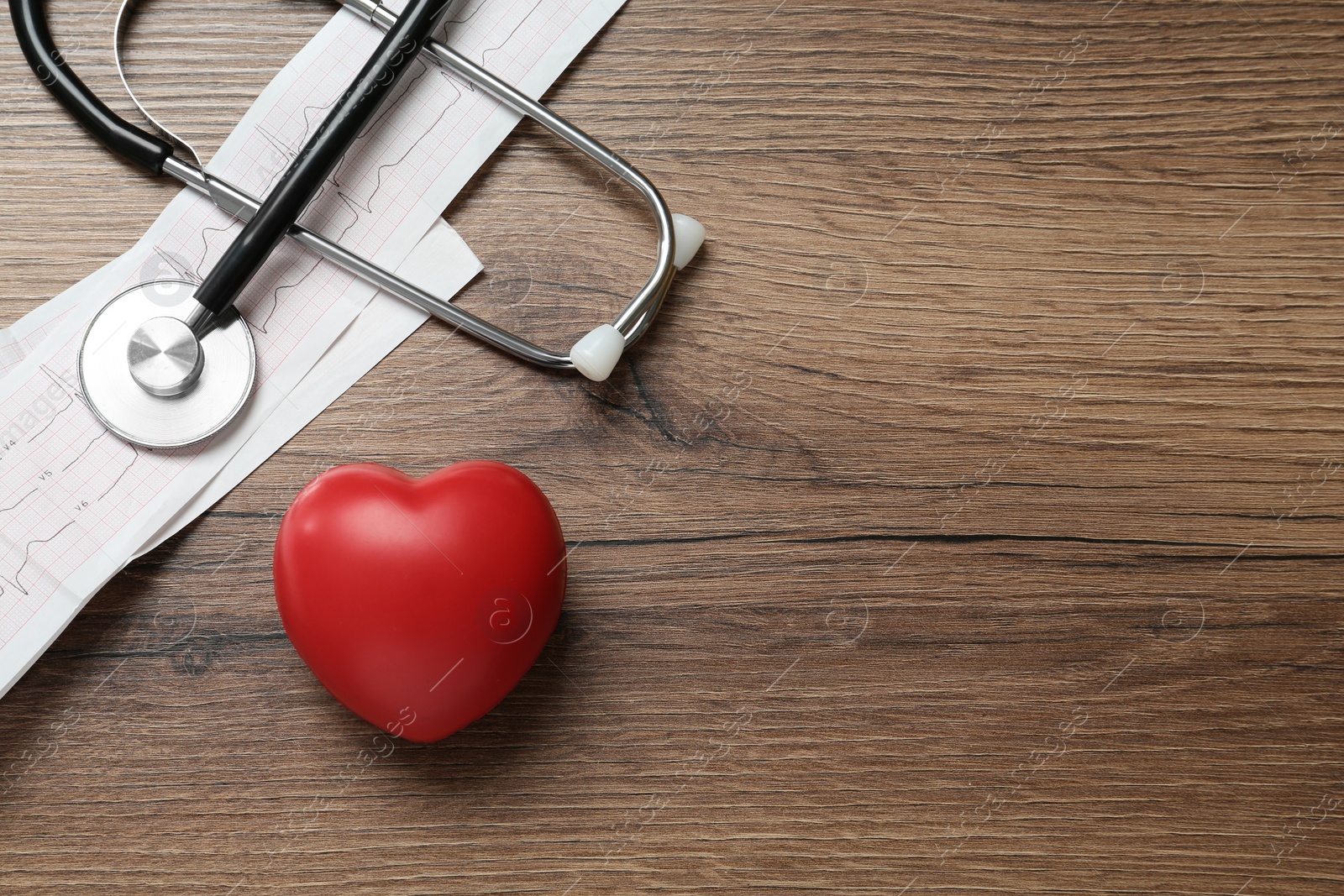 Photo of Cardiogram report, red heart and stethoscope on wooden table, flat lay. Space for text