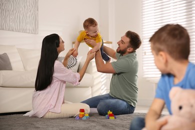 Photo of Unhappy little boy feeling jealous while parents spending time with his baby brother at home