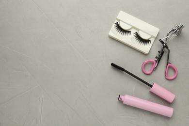 Photo of False eyelashes, curler and mascara on grey table, flat lay. Space for text