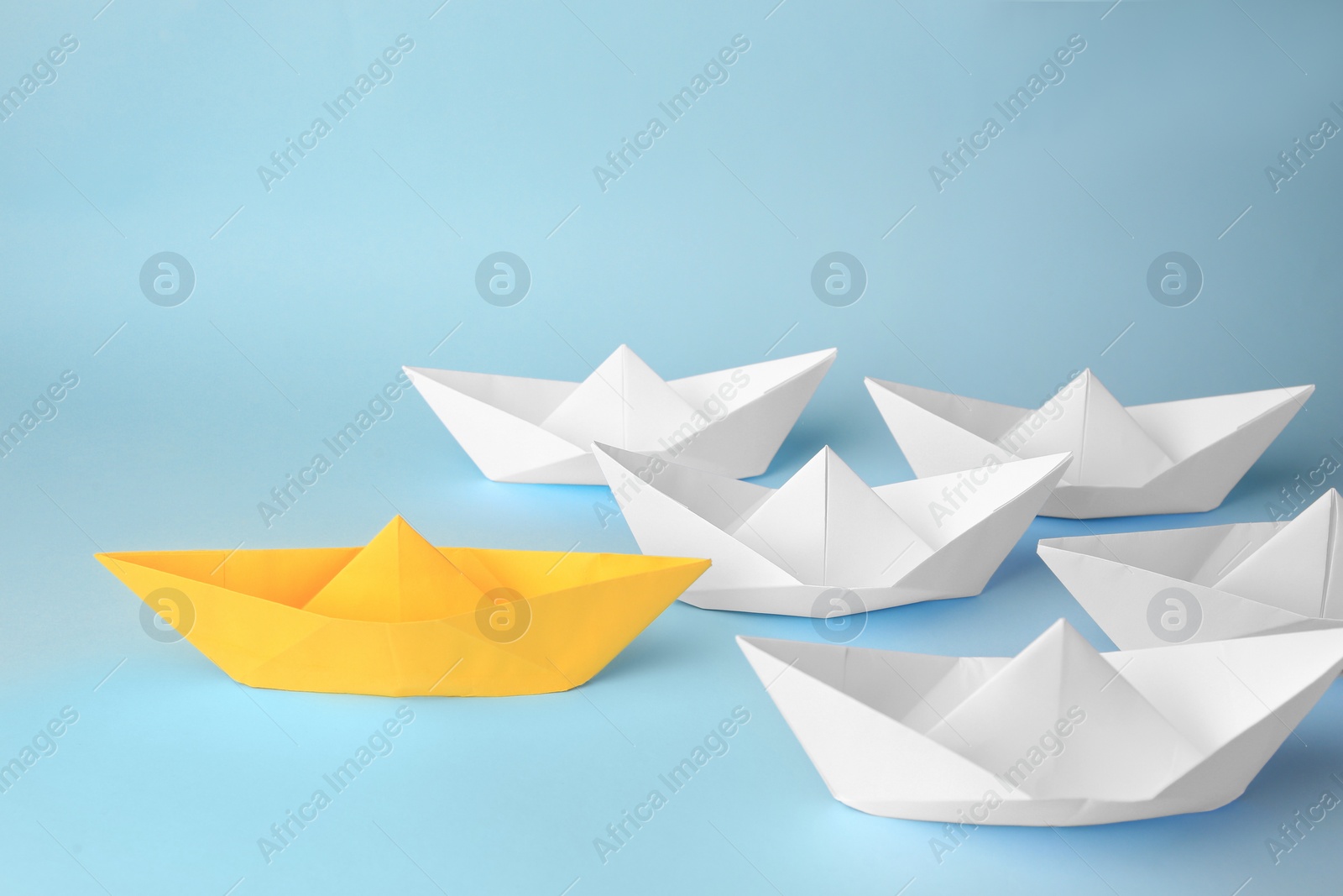 Photo of Group of paper boats following yellow one on light blue background. Leadership concept