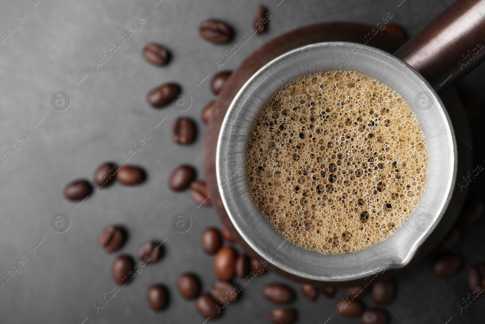 Photo of Turkish coffee in cezve and beans on grey table, top view. Space for text