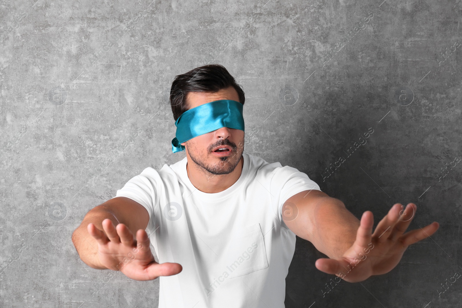 Photo of Young man wearing light blue blindfold on grey background