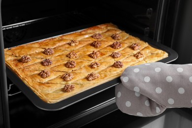 Woman taking out baking pan with delicious baklava from oven, closeup