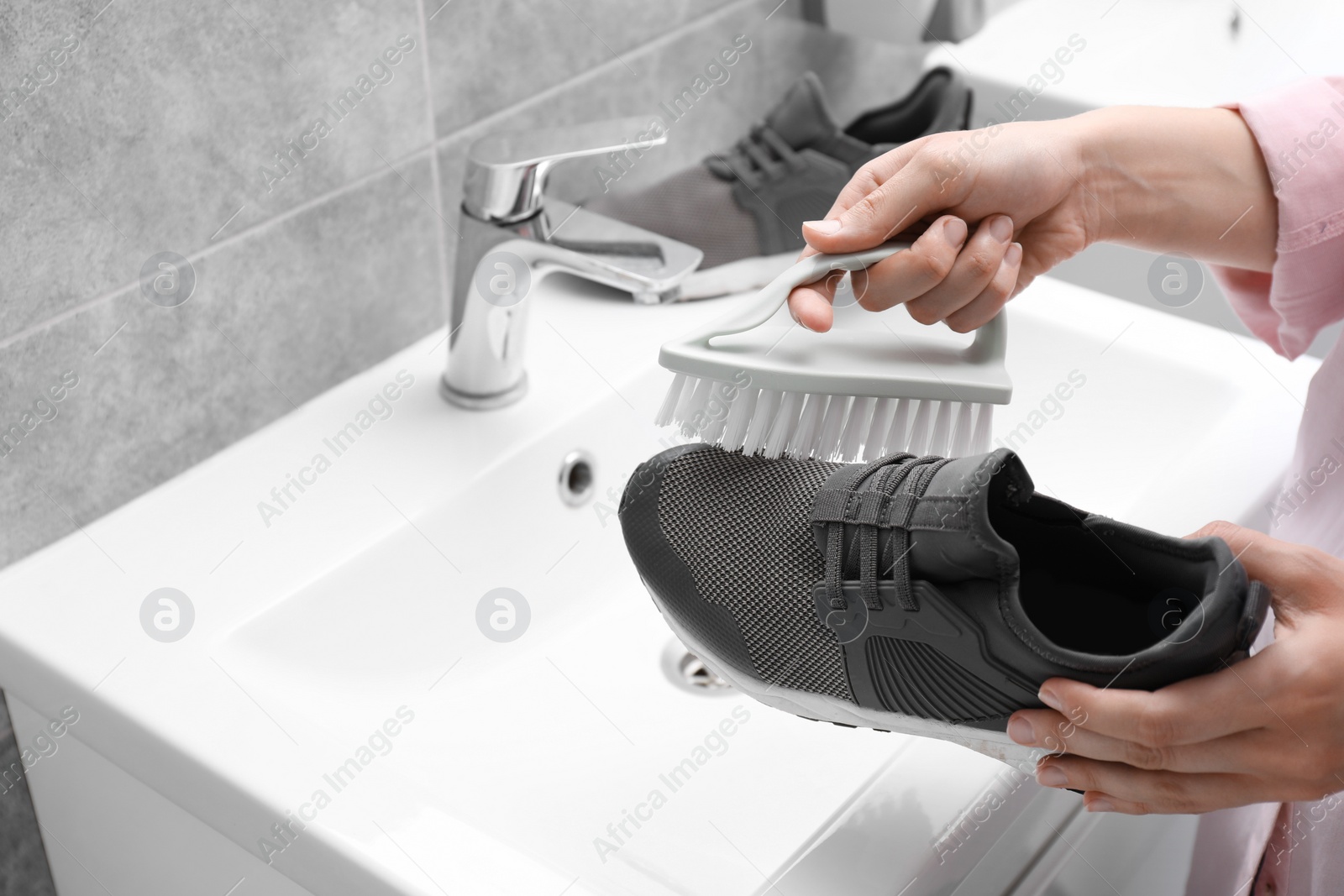 Photo of Woman washing stylish sneakers with brush in sink, closeup