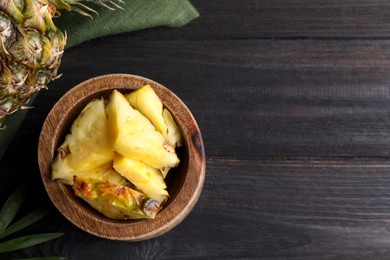 Photo of Pieces of tasty ripe pineapple in bowl on dark wooden table, flat lay. Space for text