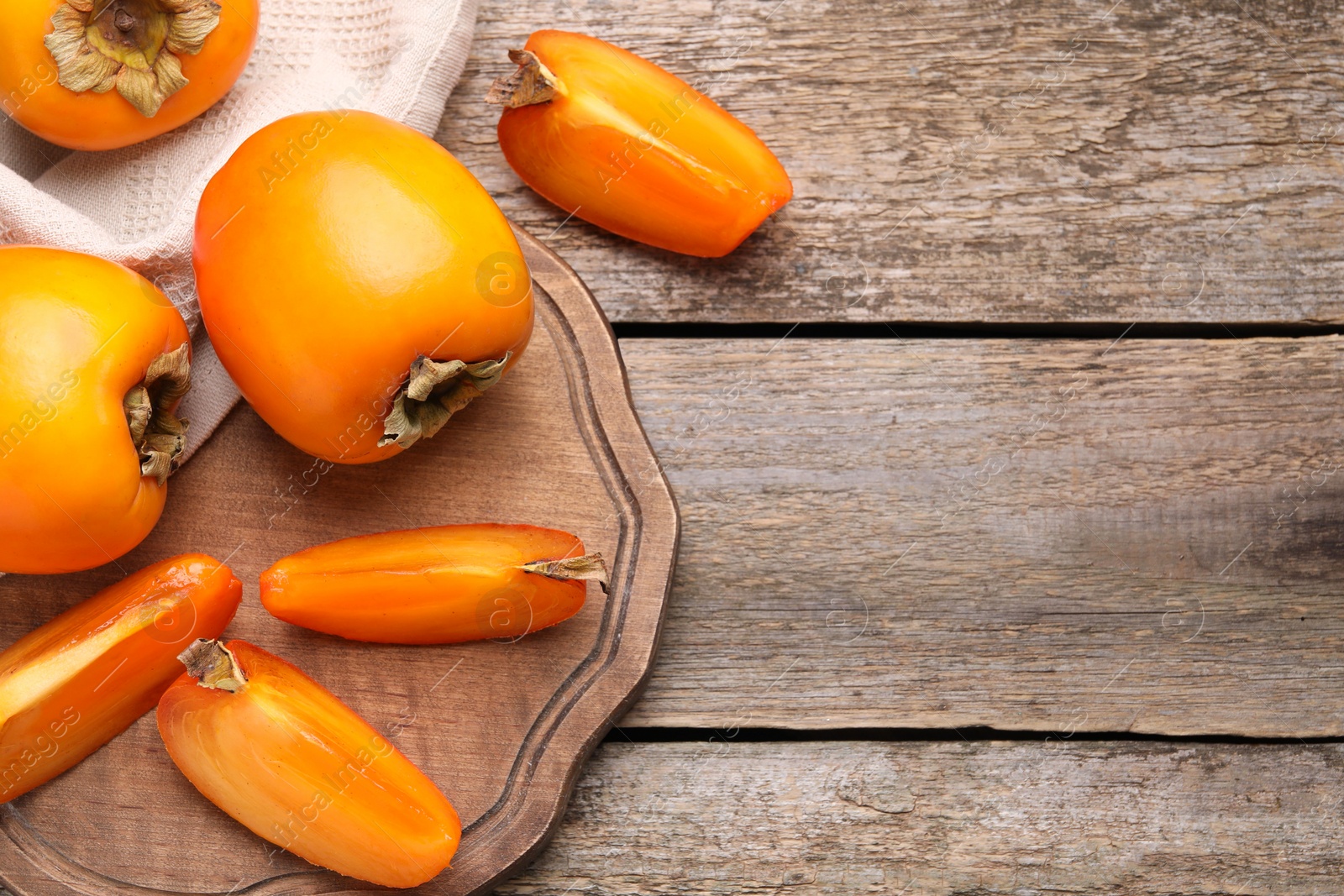 Photo of Whole and cut delicious ripe persimmons on wooden table, top view. Space for text