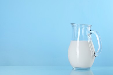 Photo of Jug of fresh milk on light blue background, space for text