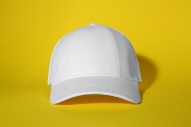 Photo of Stylish white baseball cap on yellow background