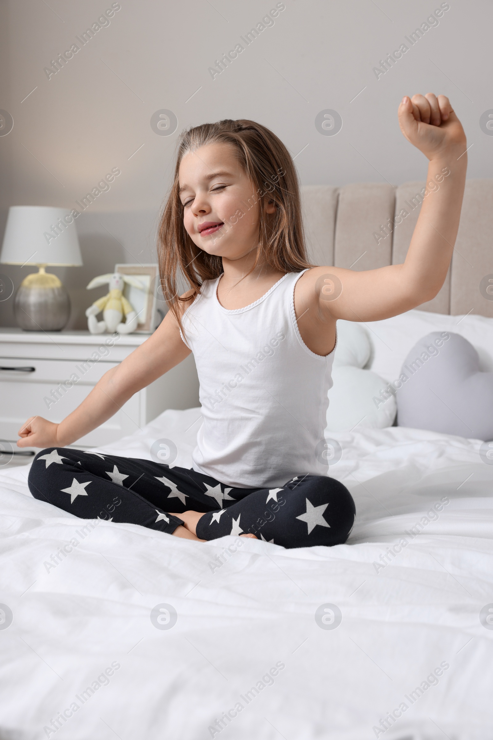 Photo of Cute little girl stretching on bed at home