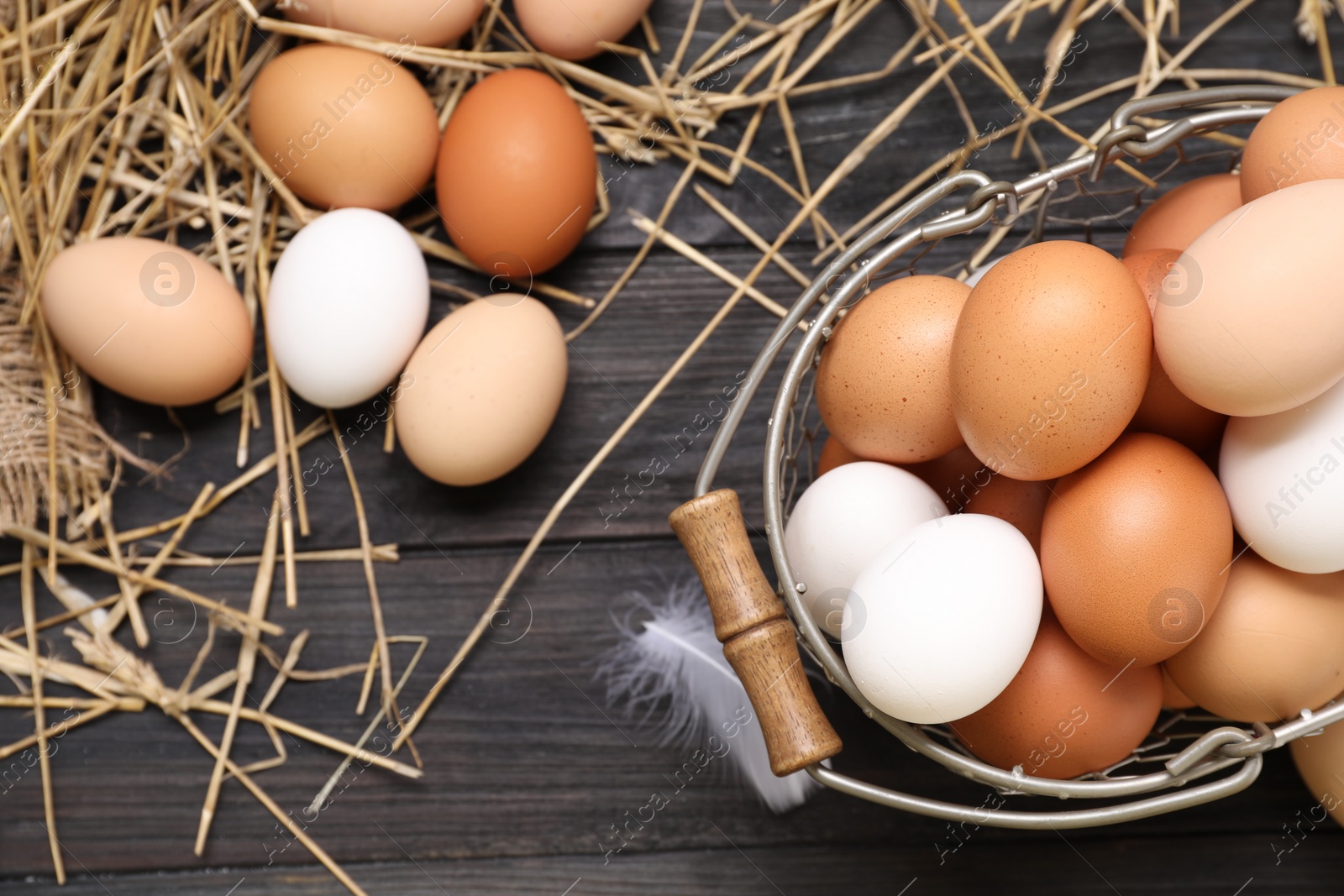 Photo of Fresh chicken eggs and dried straw on black wooden table, flat lay