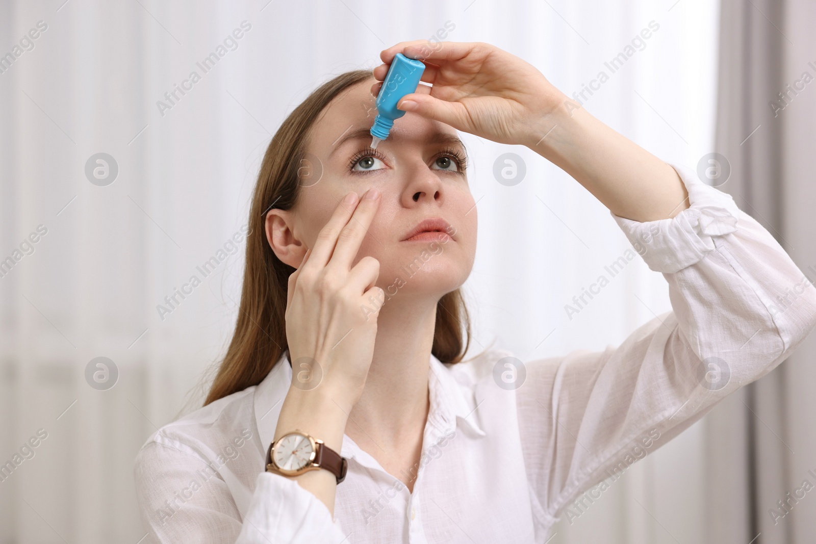 Photo of Young woman applying medical eye drops indoors